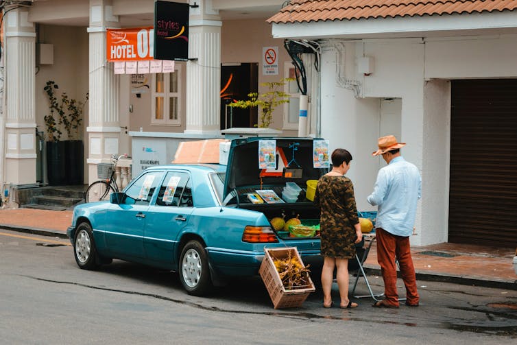 A woman buys durians out the back of a car.